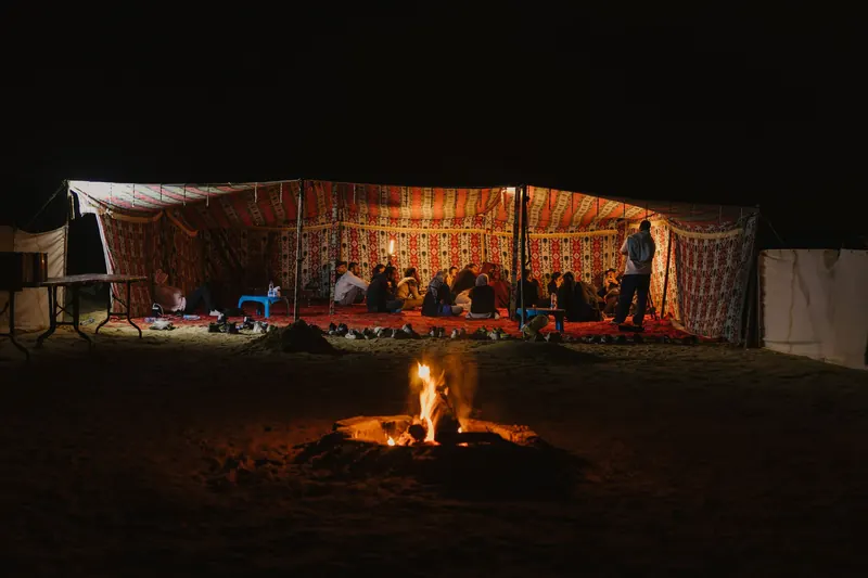 A lantern-lit desert tent with a campfire in front of it at night