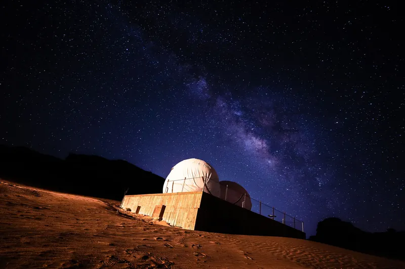 The Milky Way arching over a small observatory dome in the desert