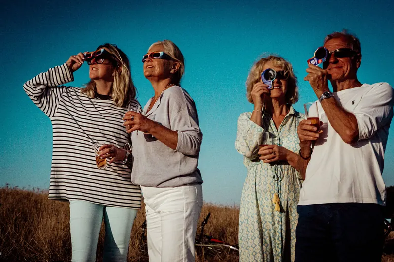 Four friends looking up at the Sun through solar eclipse glasses and a filtered camera